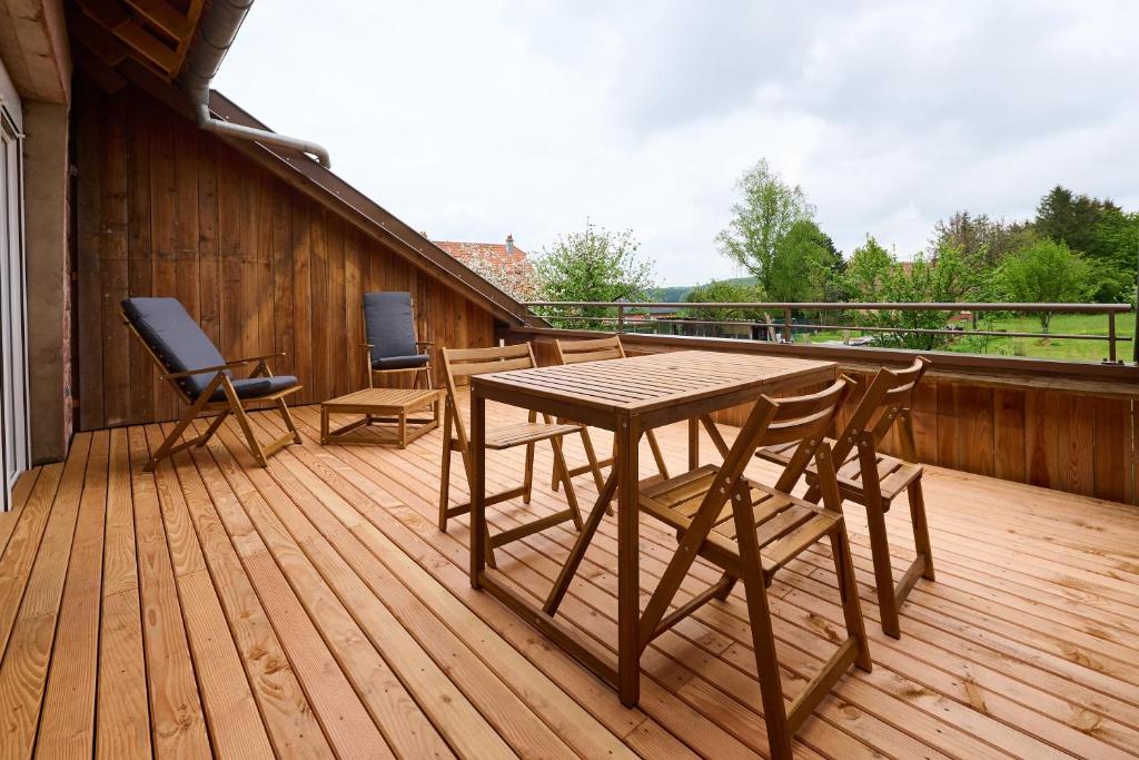 a wooden deck with a table and chairs on it at Le Noyer - Appt avec terrasse et jardin partagé in Puberg