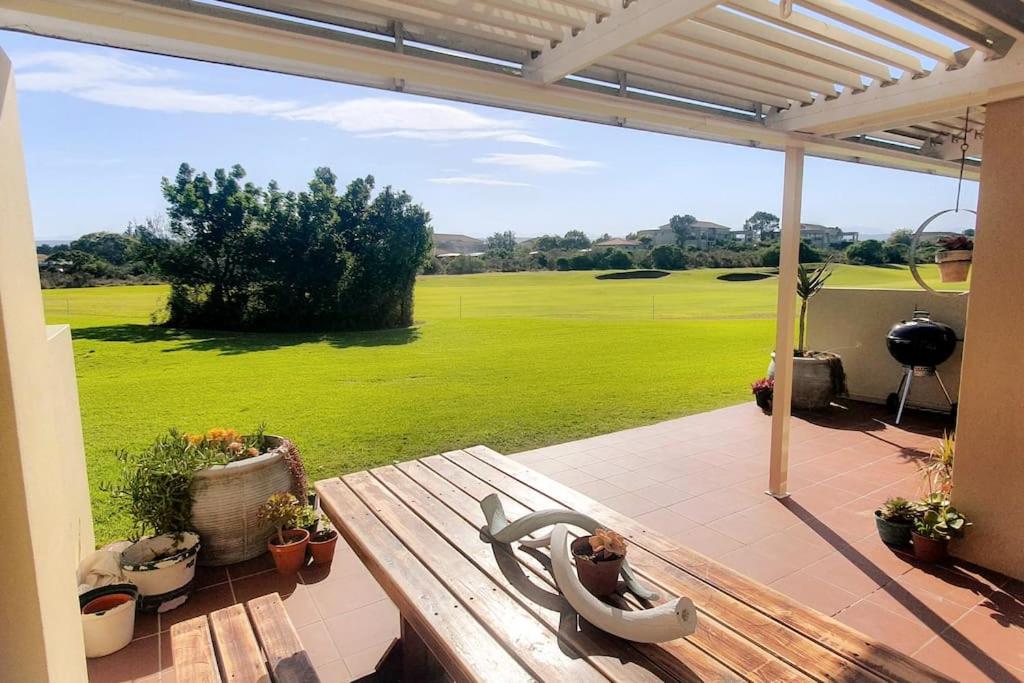 un patio con un banco y vistas a un campo verde en Sunny 2 bedroom apartment on stunning golf course, en Plettenberg Bay