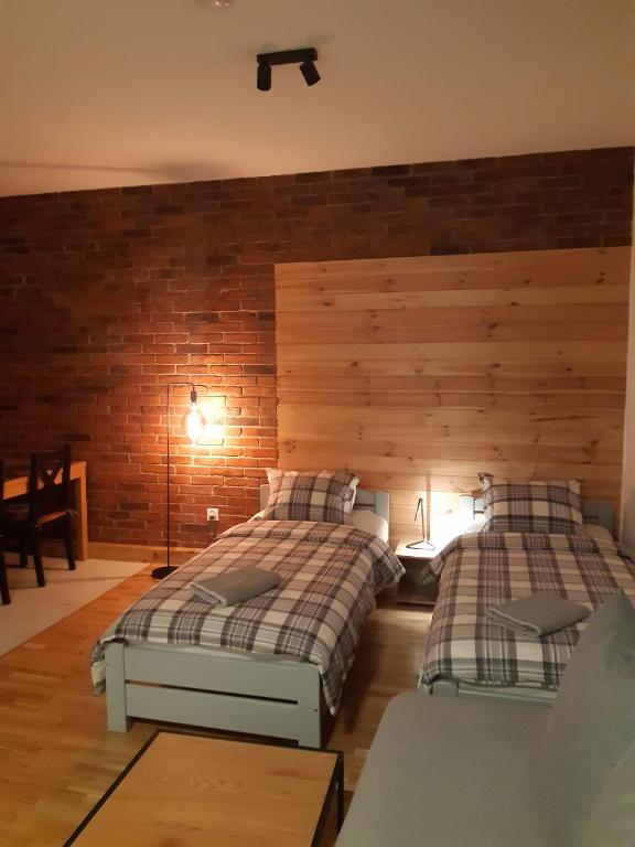 Warm-lit twin room featuring exposed brick wall, wooden headboard, two single beds and floor lamp.