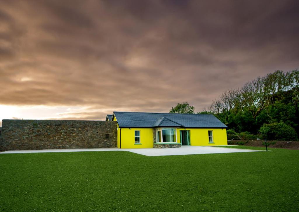 a yellow house with a wall and a green field at Carrig Island Lodge in Ballylongford