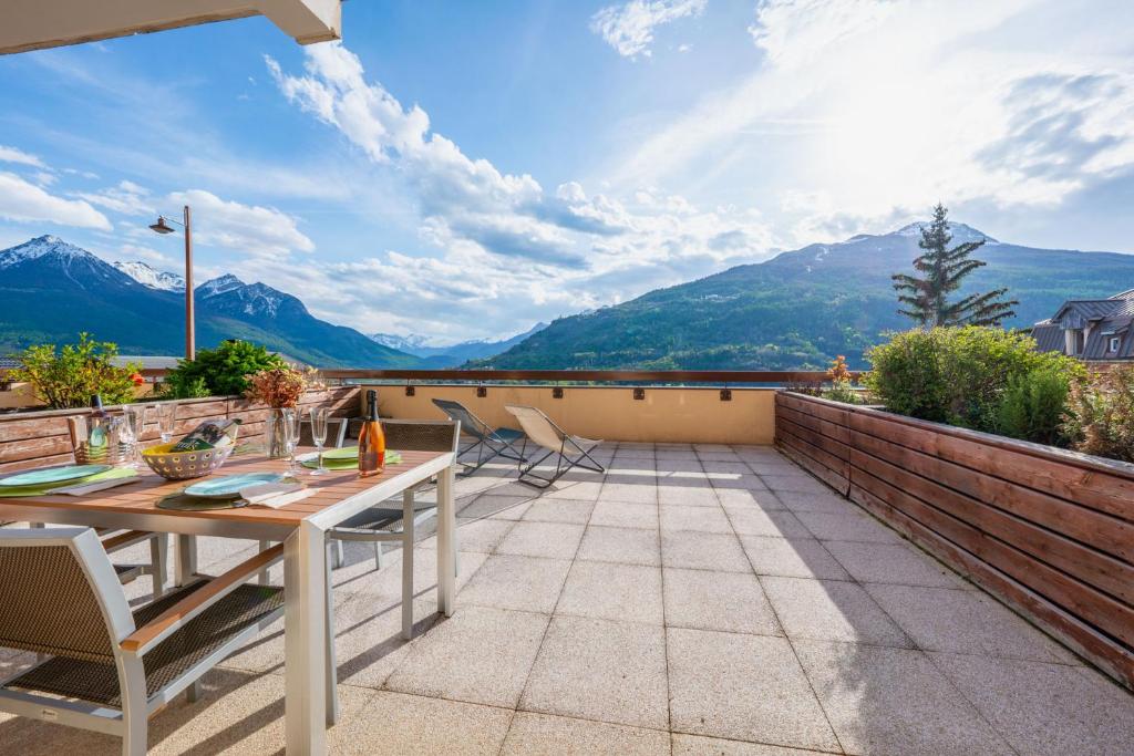 d'une terrasse avec une table, des chaises et des montagnes. dans l'établissement Le 32 Panoramique, Plein soleil, tout confort, à Briançon