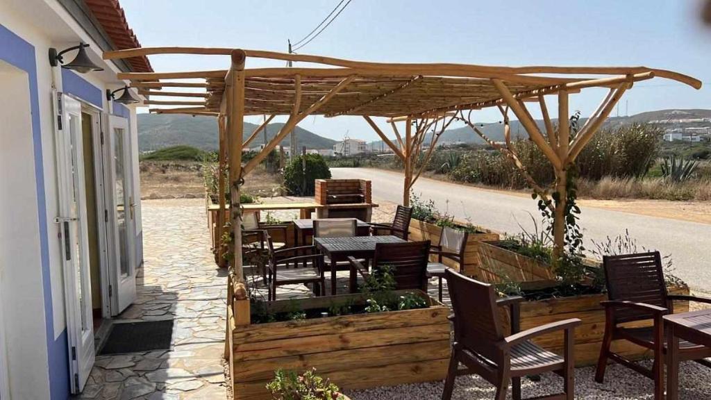 a patio with tables and chairs under a wooden pergola at Casa Presente Guesthouse in Carrapateira