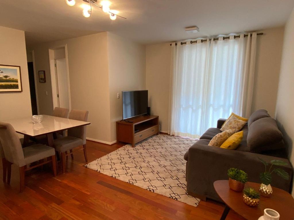 een woonkamer met een bank, een tafel en een televisie bij Apto completo e com estacionamento em Curitiba in Curitiba