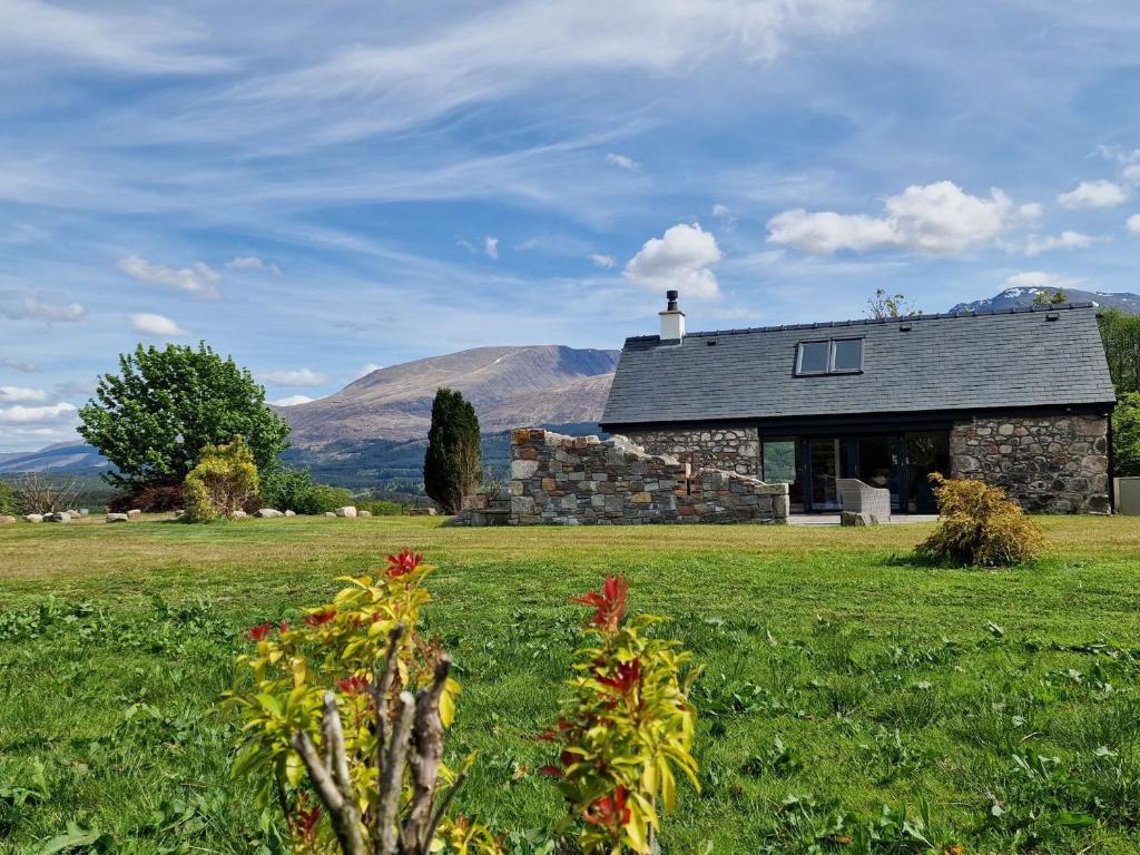 a stone house in a field with mountains in the background at The Barn in Fort William