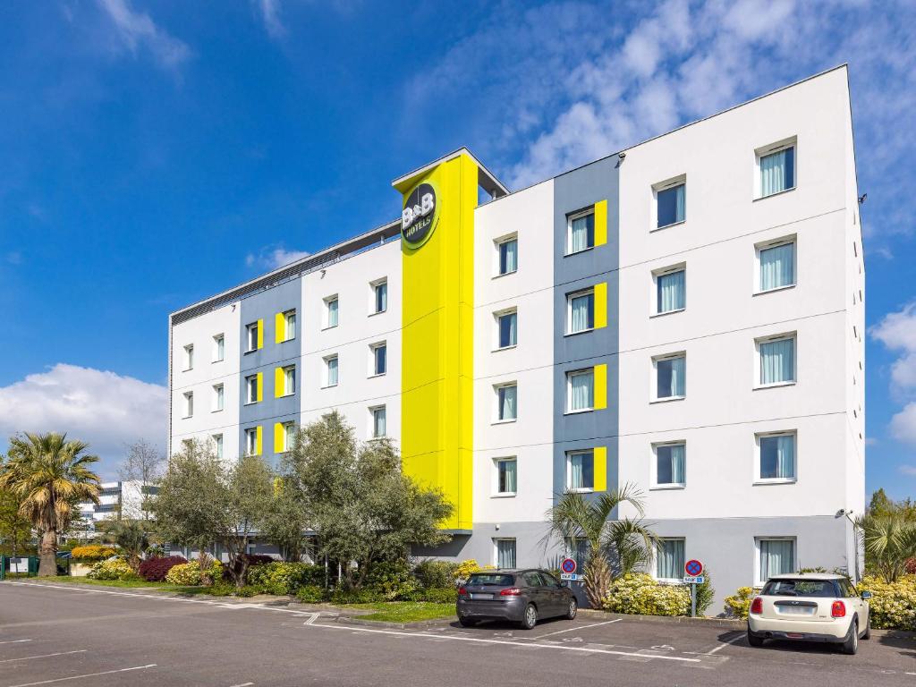 un bâtiment jaune et blanc avec une horloge. dans l'établissement B&B HOTEL Rennes Ouest Villejean, à Rennes