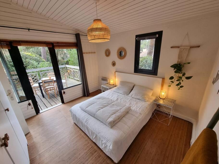 une chambre avec un grand lit blanc et un balcon dans l'établissement Charmant cottage dans les pins, entre océan & golf, à Lacanau