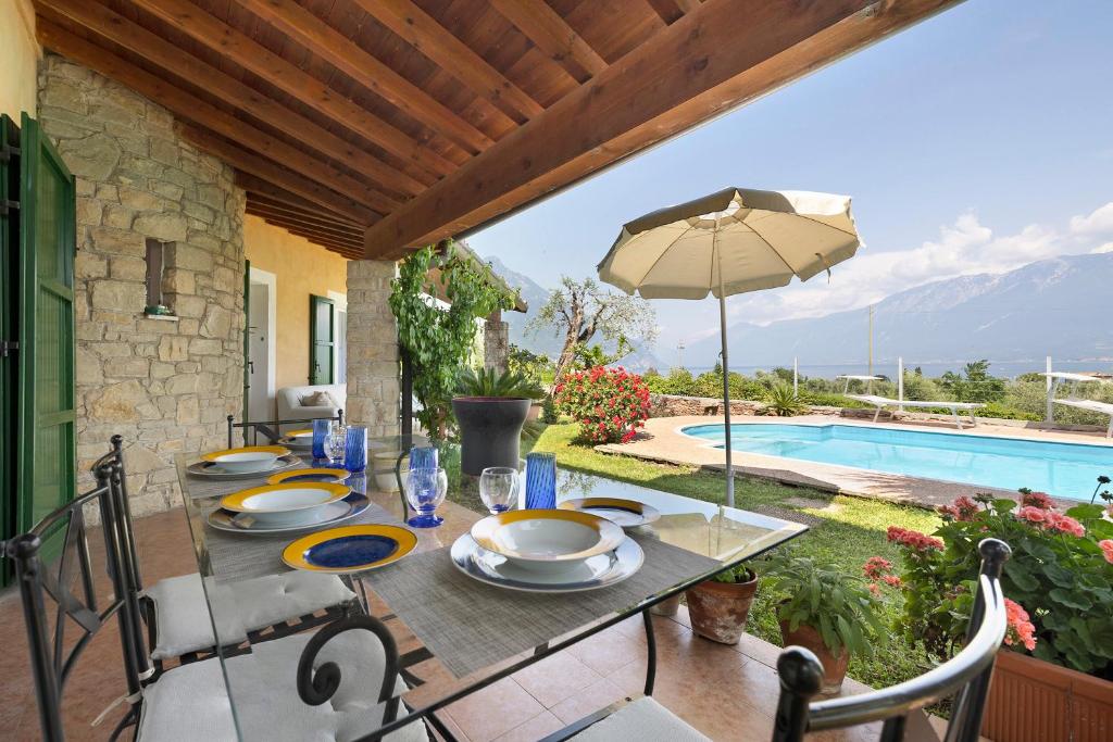 een tafel met stoelen, een parasol en een zwembad bij Villa Corneghe in Gargnano