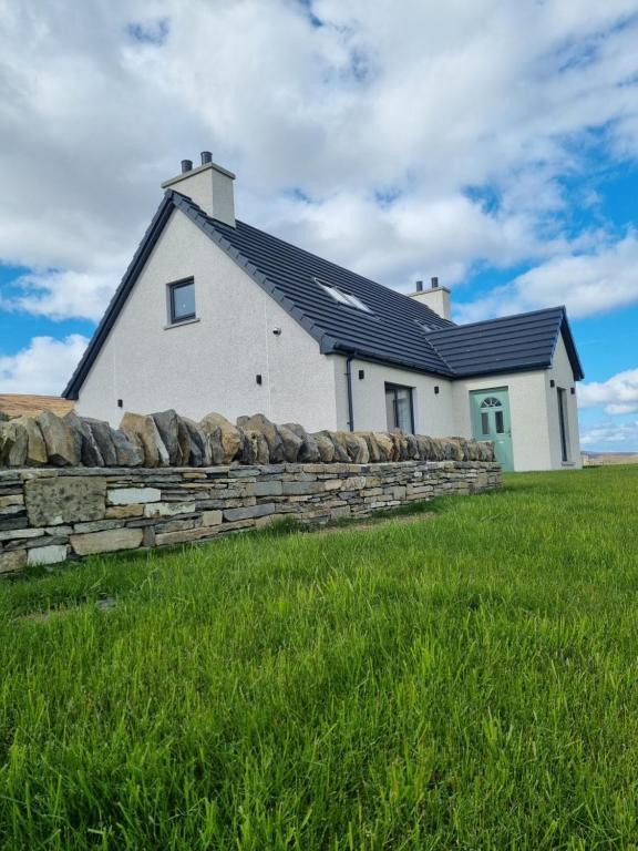 a white house with a stone wall in a field at Redland Cottage in Orkney