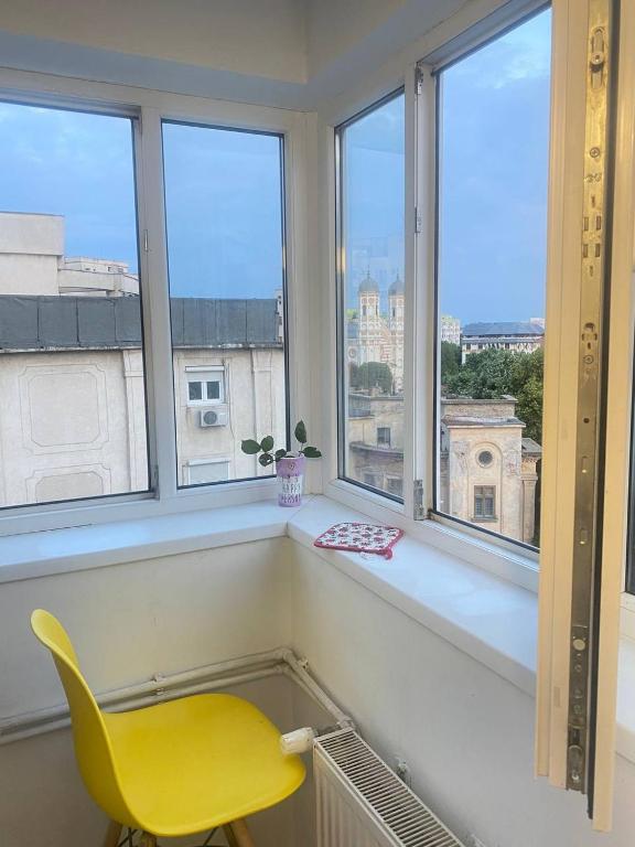 a yellow chair sitting in a room with windows at Private room at Ceausescu's place in Old City Unirii Square in Bucharest