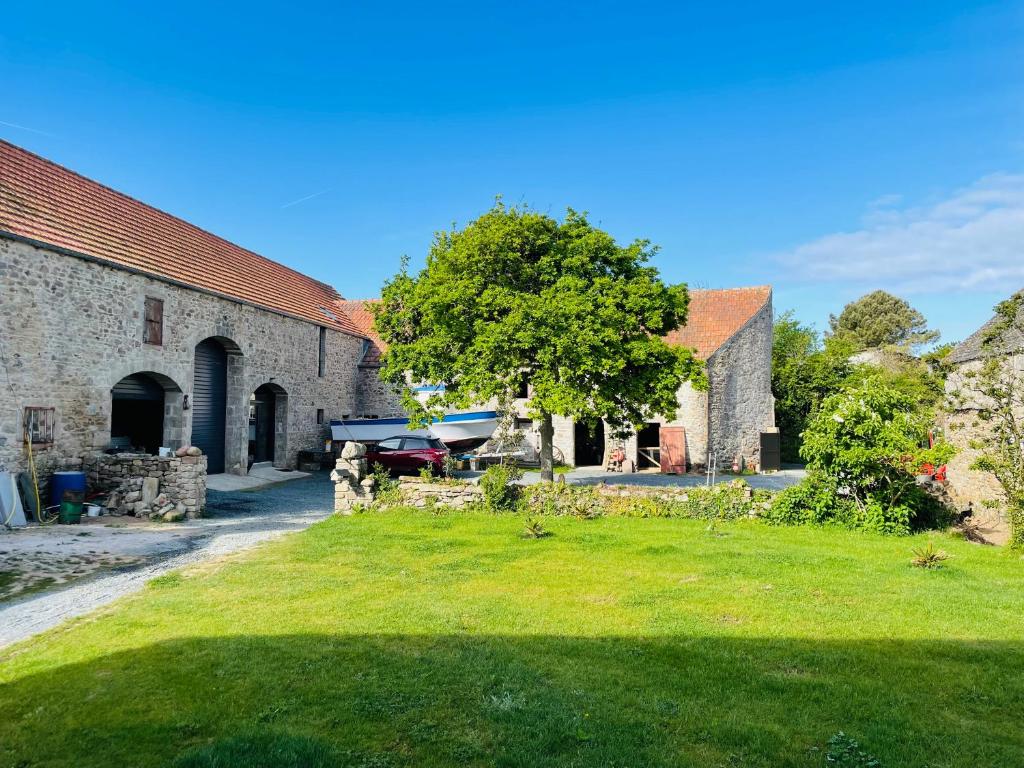 - un vieux bâtiment en pierre avec un arbre dans la cour dans l'établissement La Ferme du Raz Blanchard, à Auderville