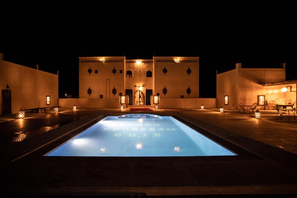 a large swimming pool in front of a building at night at Riad Merzouga Dunes in Merzouga