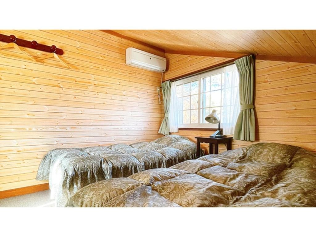two beds in a room with wooden walls and a window at Hakuba Pension Meteor - Vacation STAY 63342v in Hakuba