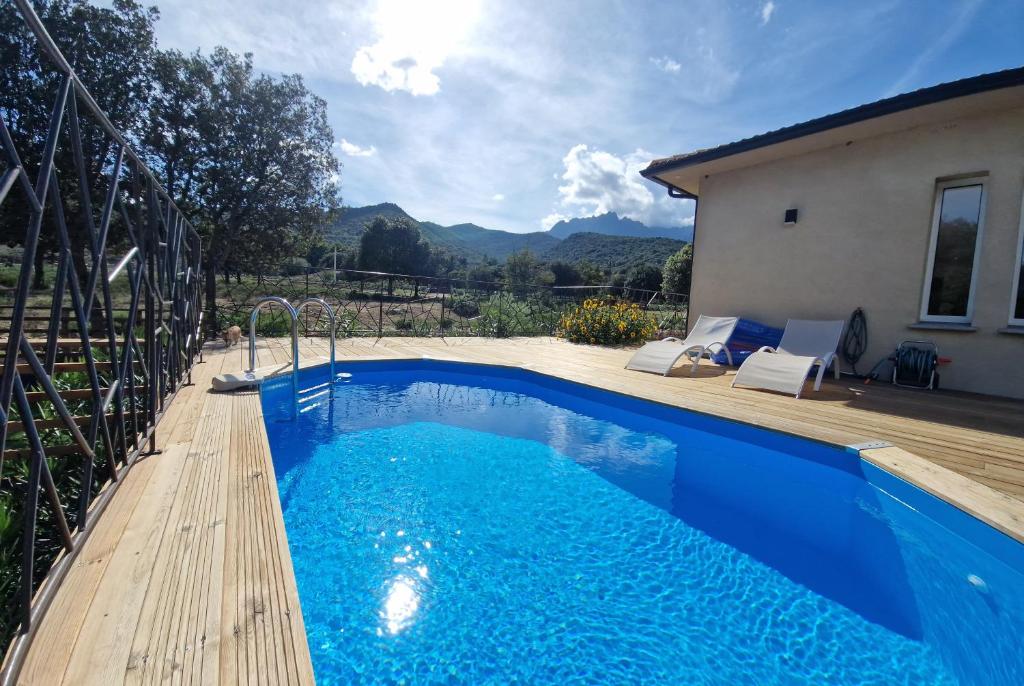 ein blauer Pool mit einer Holzterrasse neben einem Haus in der Unterkunft Domaine U Filanciu - Maison Chiara avec piscine - Centre Corse in Moltifao