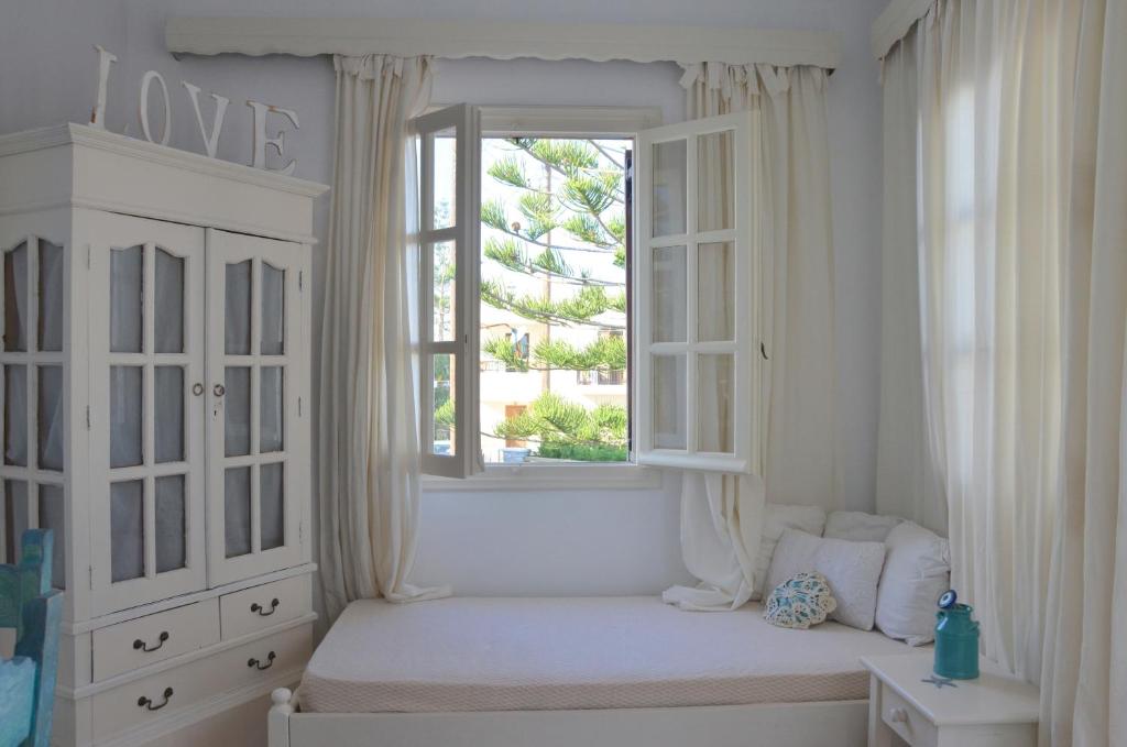 Cette chambre blanche dispose d'une fenêtre et d'un lit avec un siège de fenêtre. dans l'établissement ANIMA family apartment, à Naxos Chora
