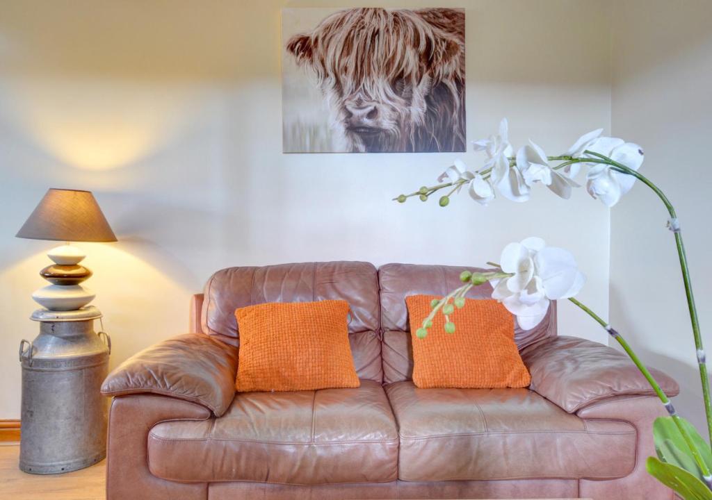 a brown leather couch with orange pillows in a living room at Y Beudy in Y Felinheli
