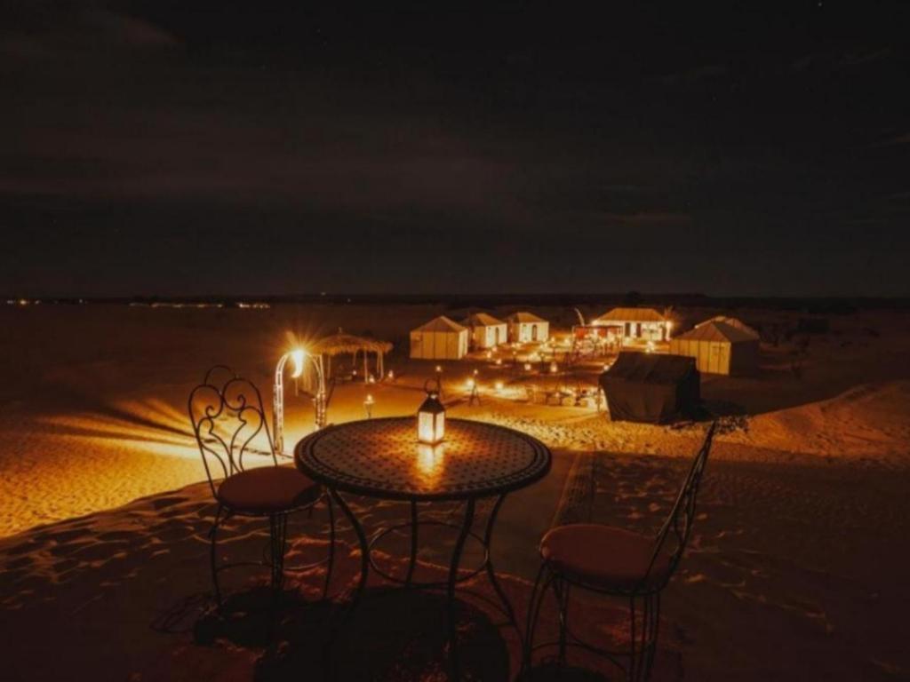 Desert Coast Opulent Camp في مرزوقة: طاولة وكراسي على الشاطئ في الليل