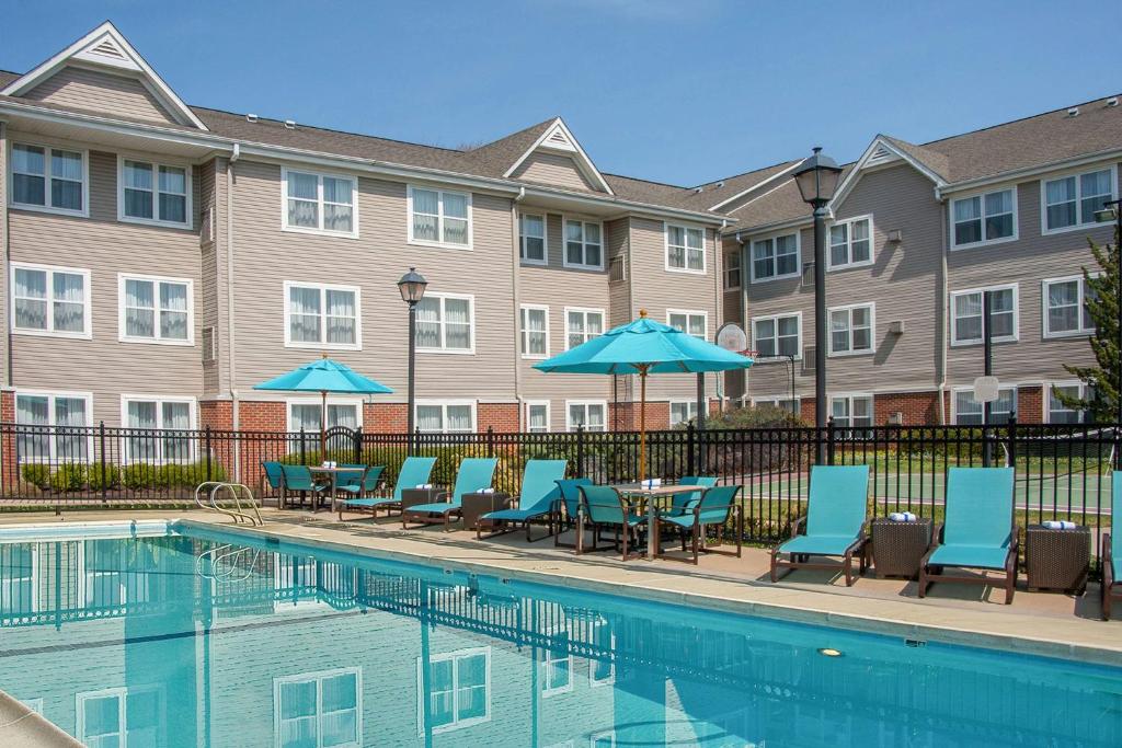 einen Pool mit Stühlen und Sonnenschirmen neben einem Gebäude in der Unterkunft Sonesta ES Suites Charlottesville University in Charlottesville