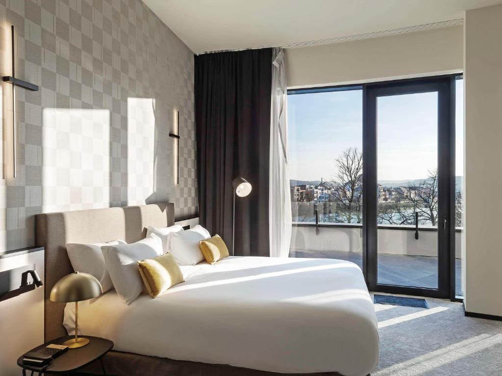 a bedroom with a large white bed and a large window at Mercure Namur Hotel in Namur