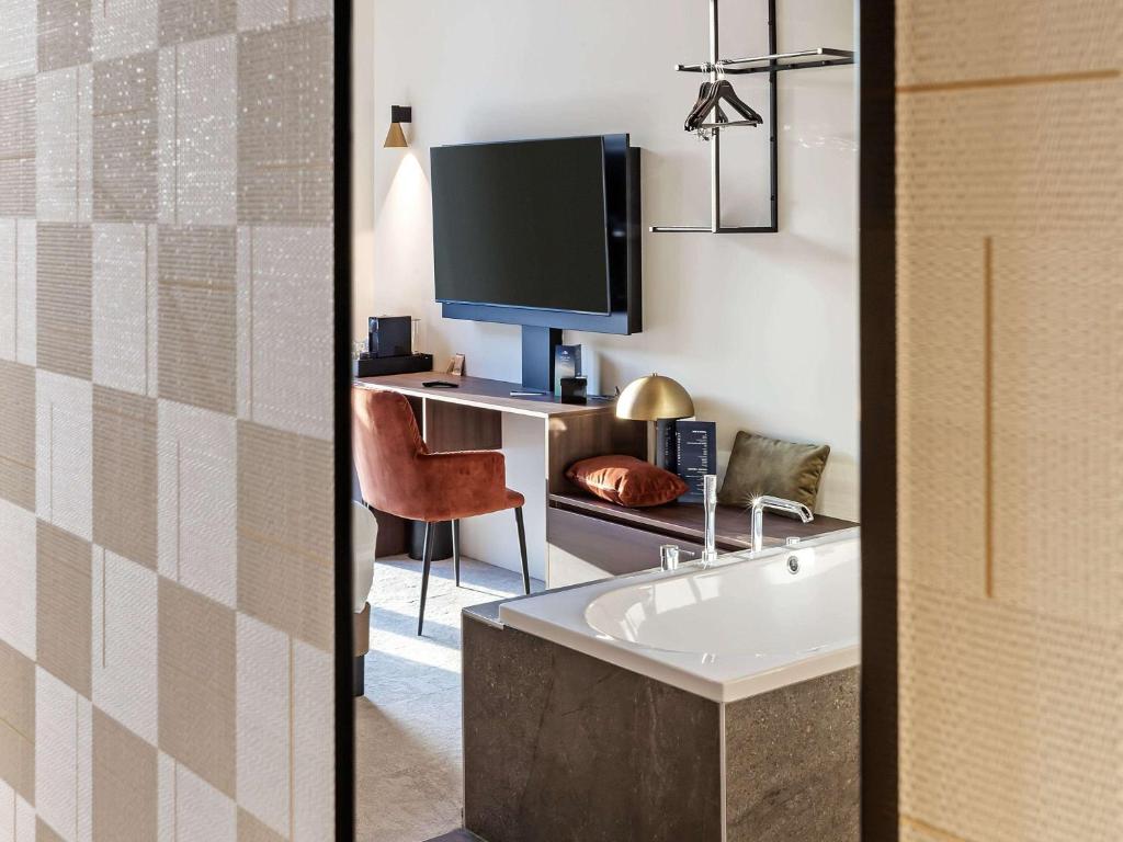 a bathroom with a tub and a desk with a tv at Mercure Namur Hotel in Namur