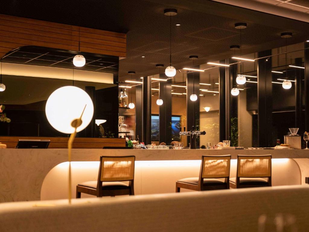 a restaurant with three chairs and a bar with lights at Mercure Namur Hotel in Namur