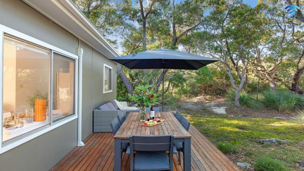 a wooden table with an umbrella on a deck at Kangaroo Cottage in Currarong