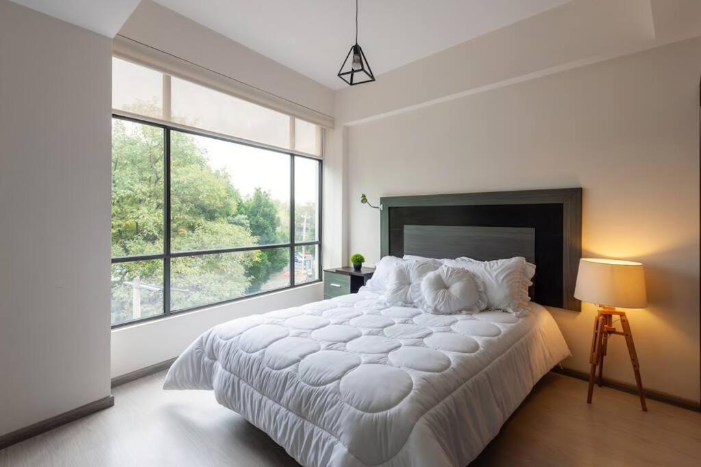 a white bedroom with a large bed and a large window at Central and cozy CDMX 1BR in Mexico City