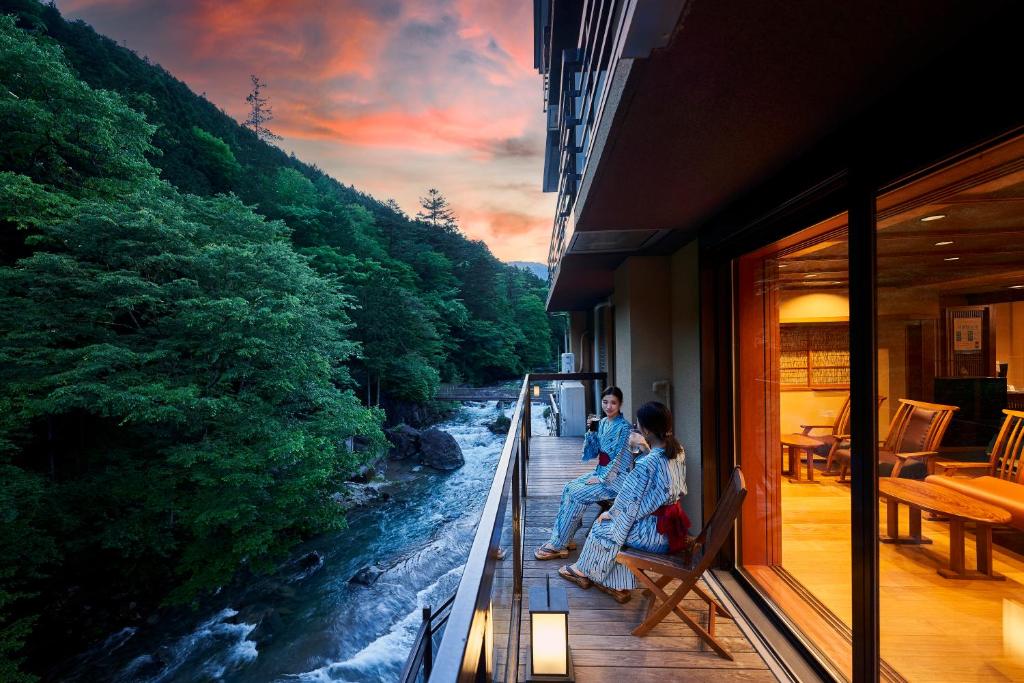 two people sitting on a balcony looking at a river at Shima-Onsen Toshimaya in Nakanojo