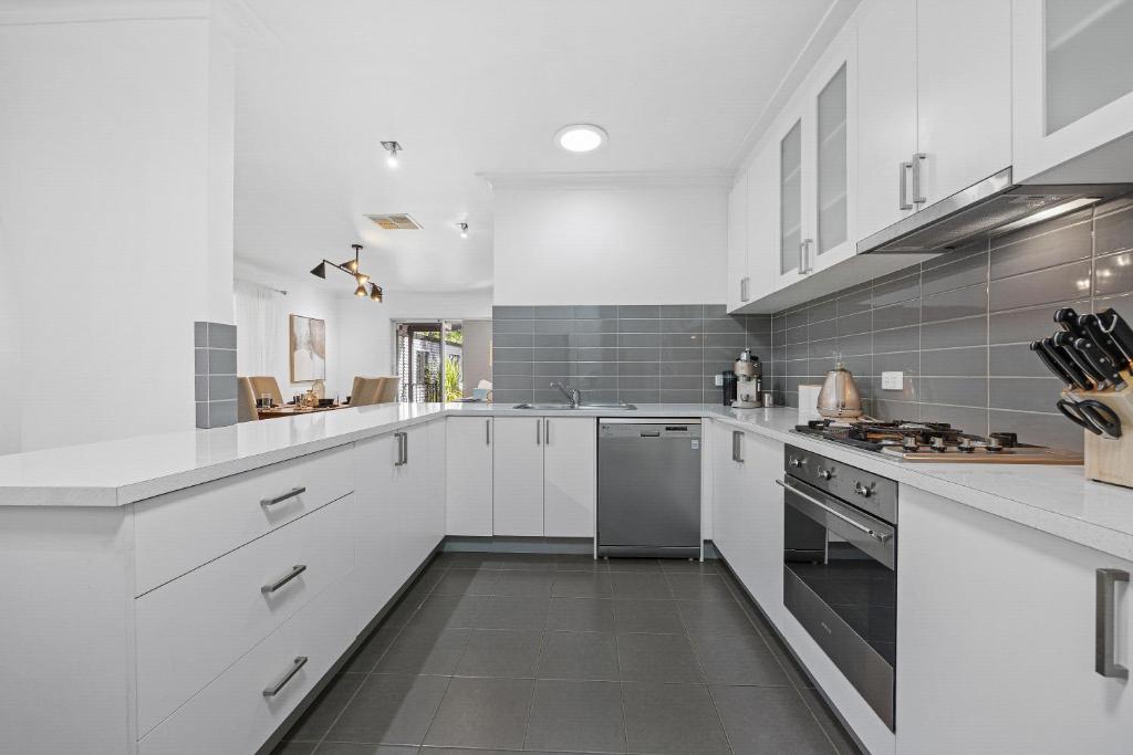 a white kitchen with white cabinets and appliances at Cozy Cottage for Families, Sleeps 8 , Big backyard, parking for 4 cars, Walking distance to Shopping mall in Ballarat