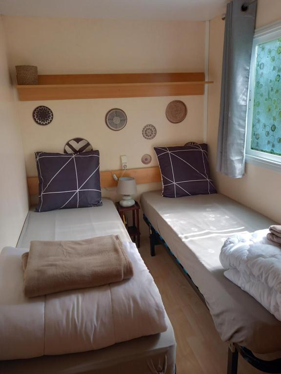 Habitación con 2 camas con almohadas moradas y ventana. en Mobile home au camping les Tilleuls du Caminel, en Sarlat-la-Canéda