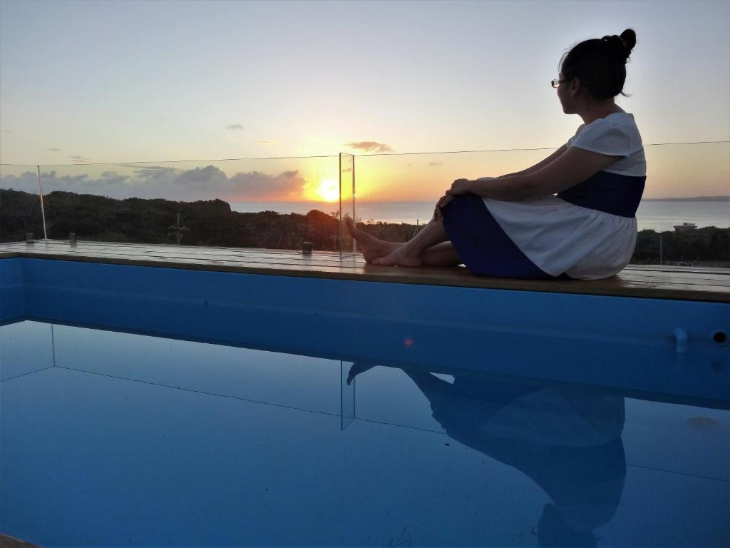 una mujer sentada en el borde de una piscina viendo la puesta de sol en La Maison B&B en Eluan
