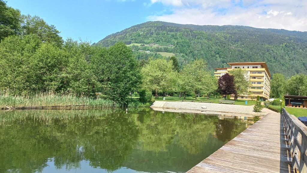 un puente de madera sobre un lago con un edificio en el fondo en ELISABETH Haus KMB Seeappartement direkt am Ossiacher See mit Hallenbad Skiarena Gerlitzen en Bodensdorf