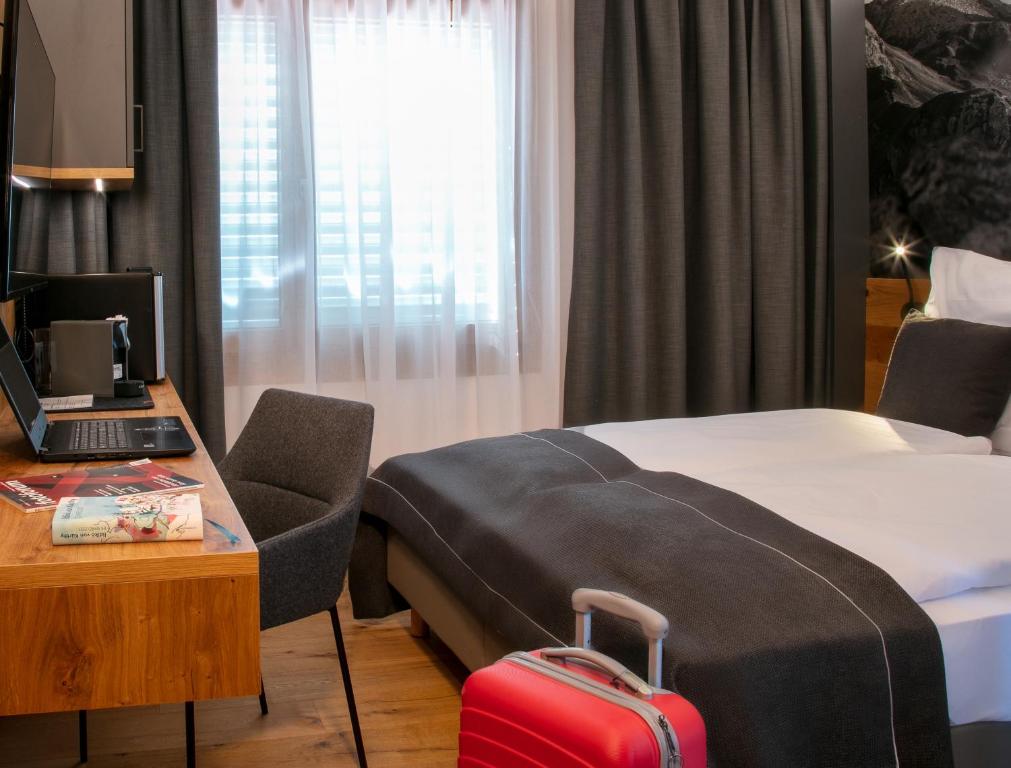 a hotel room with a bed and a desk with a suitcase at Landhaus Boutique Motel - contactless check-in in Nendeln