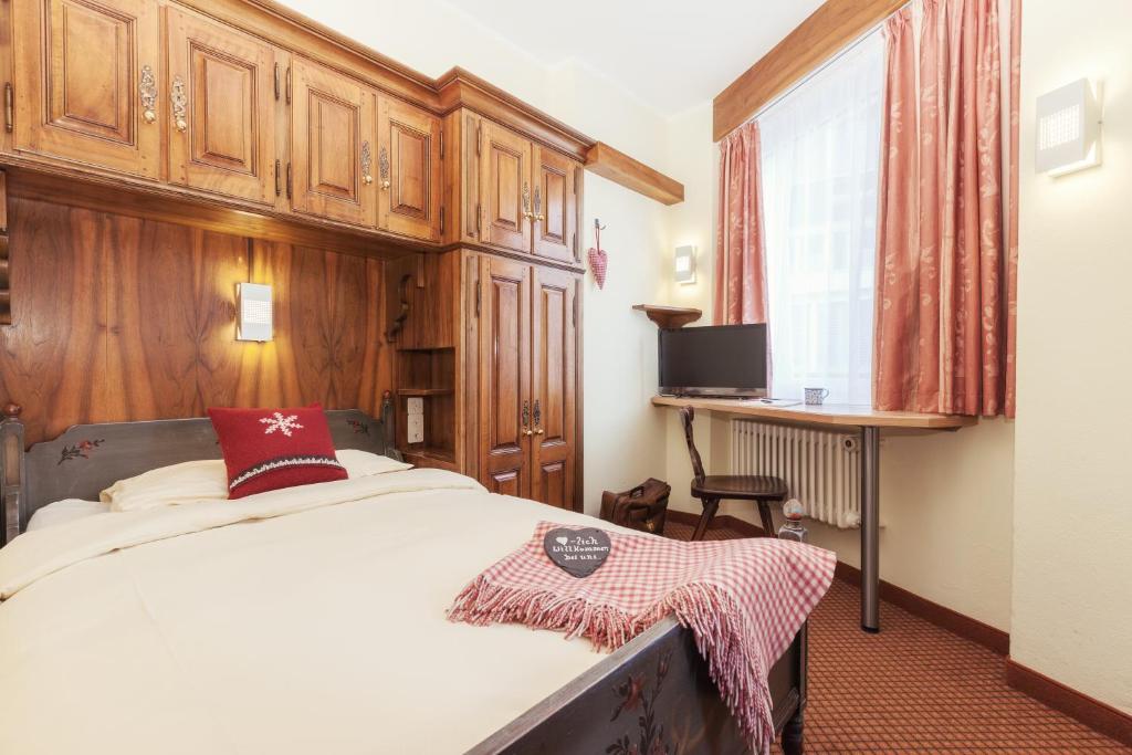 a bedroom with a bed and a desk and a window at Le Petit CHARME-INN in Zermatt