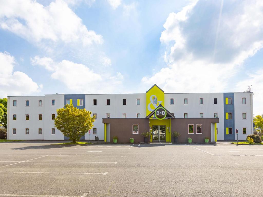 a large white building with a parking lot at B&B HOTEL Rennes Est Cesson Sévigné in Cesson-Sévigné