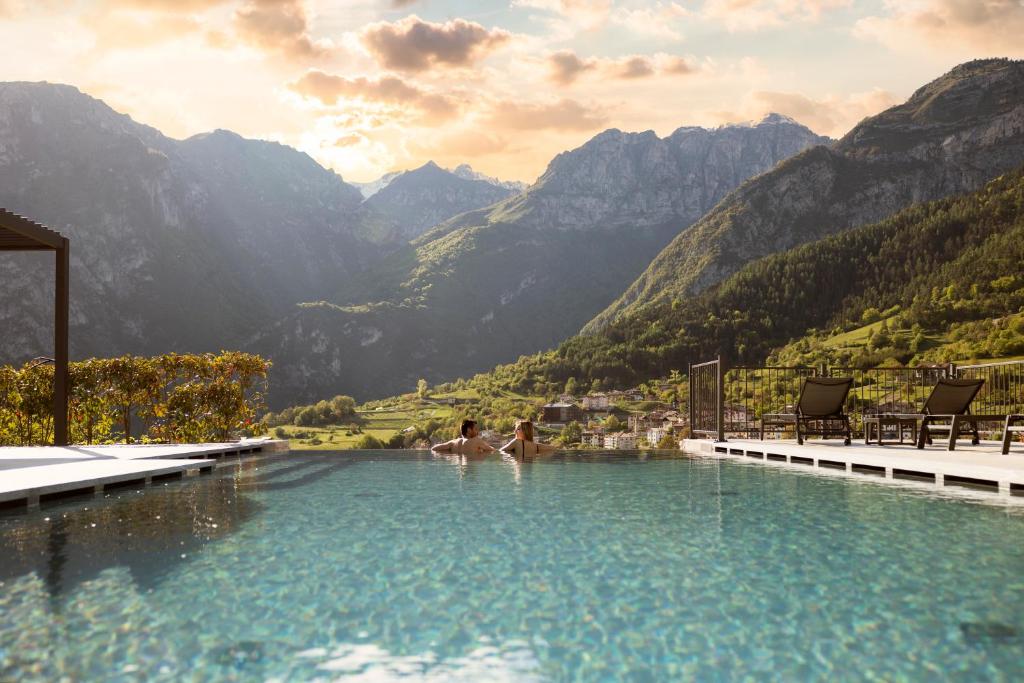 due persone che nuotano in una piscina con montagne sullo sfondo di Hotel Castel Mani a San Lorenzo in Banale