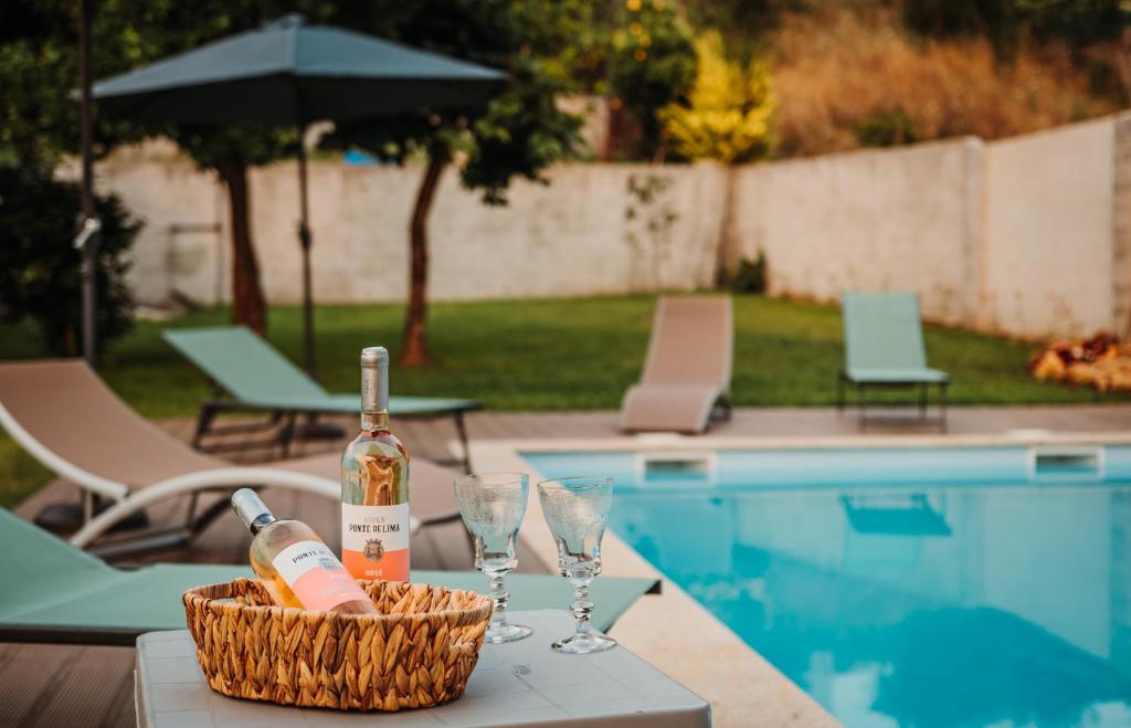 una bottiglia di vino e bicchieri su un tavolo accanto alla piscina di Villa Henriques a Ponte de Lima