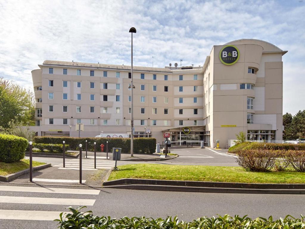 un grand bâtiment avec un parking en face de celui-ci dans l'établissement B&B HOTEL Paris Roissy CDG Aéroport, à Roissy-en-France