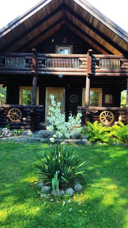 a log cabin with a porch and flowers in the yard at Gojaus smukle in Molėtai