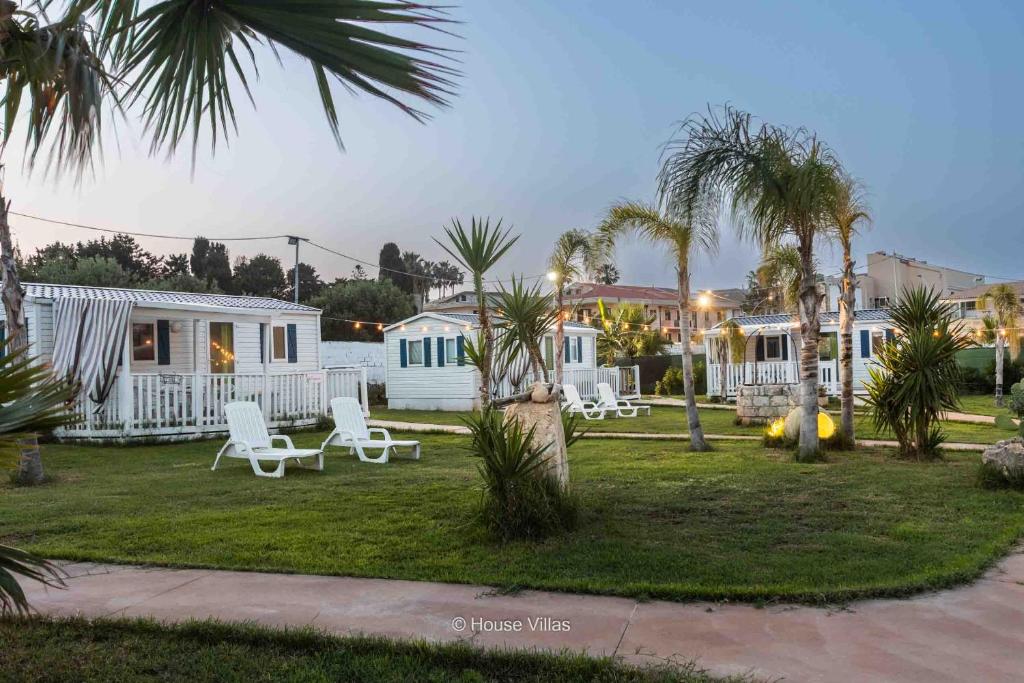 un patio del complejo con sillas blancas y palmeras en House&Villas - Residence Il Borgo, en Avola