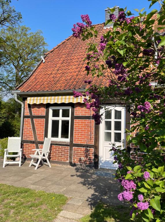 a red brick house with two white chairs and flowers at Altes Waldarbeitergehöft in Munster