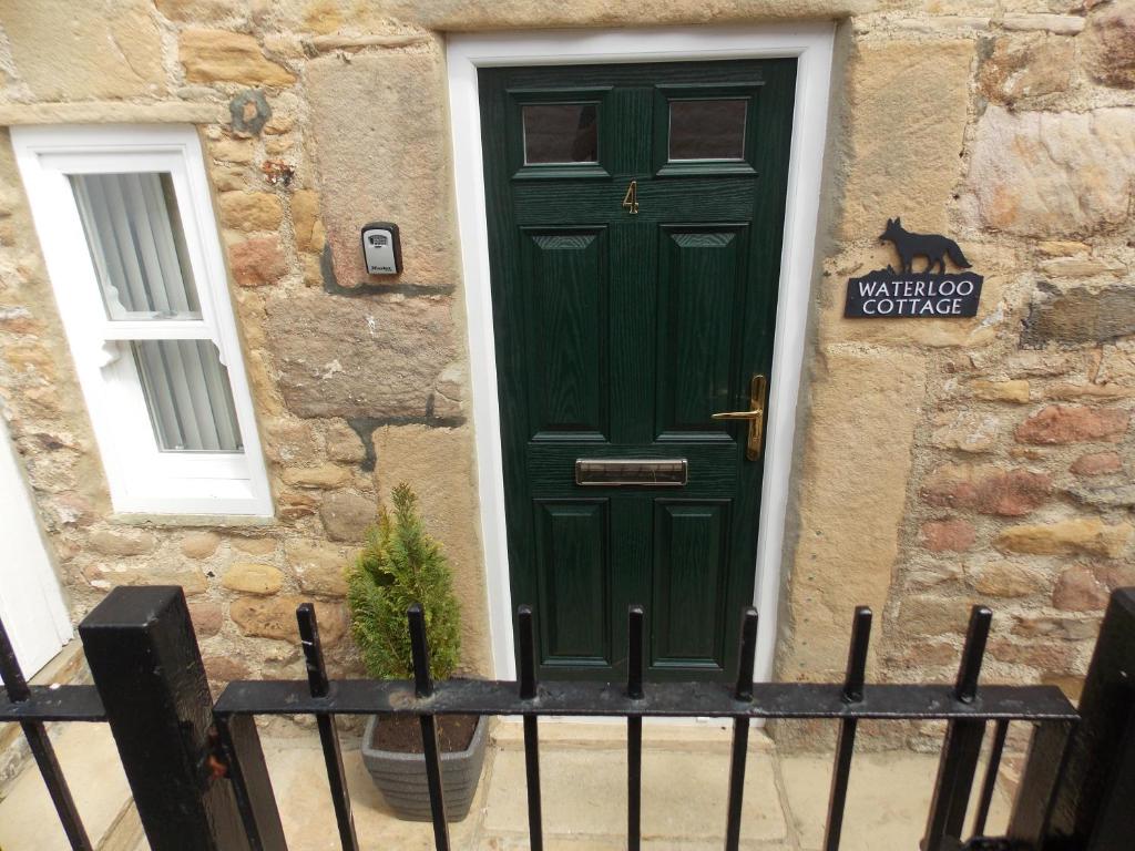 a green door on a stone building with a cat on it at Waterloo Cottage in Barnard Castle