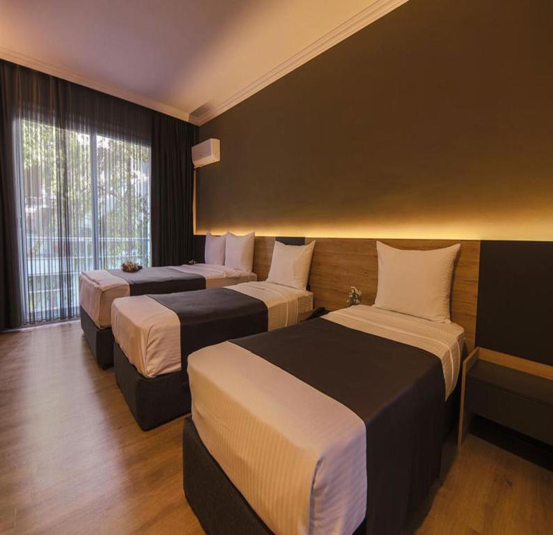 a hotel room with three beds and a window at Grand Faik Hotel in Cesme