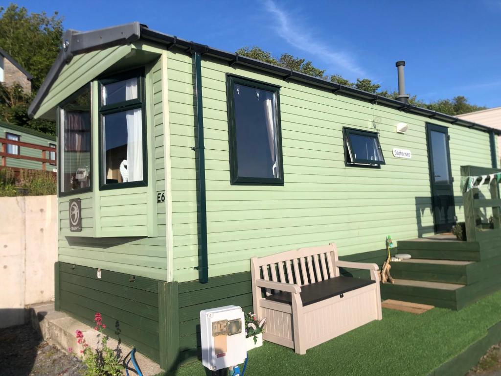 a green tiny house with a bench in the yard at Cosy holiday caravan minutes from the beach in Aberystwyth
