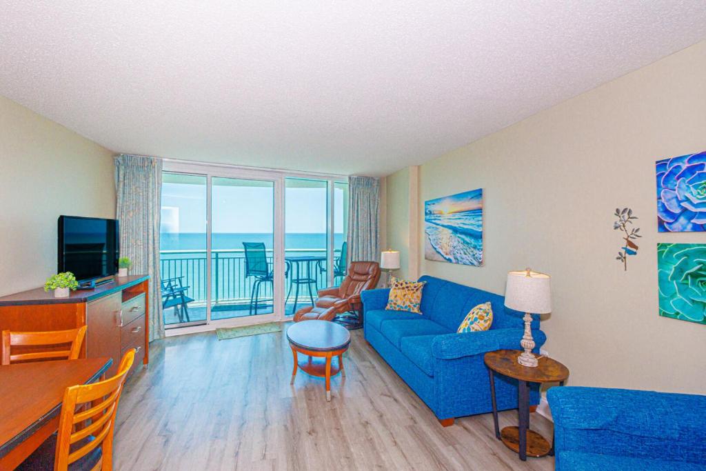 a living room with a blue couch and a balcony at Direct Oceanfront Condo-Sandy Beach Resort 1610- Sleeps 6! in Myrtle Beach