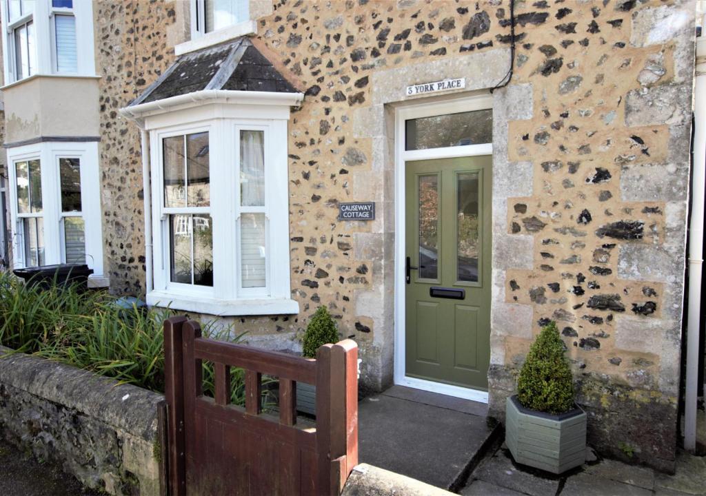 um edifício de pedra com uma porta verde e um banco em Causeway Cottage em Beer