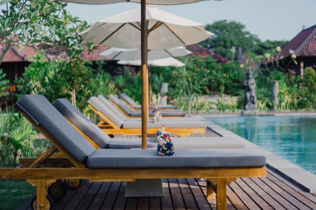 a row of lounge chairs with an umbrella next to a pool at Sunset Star Huts in Nusa Lembongan