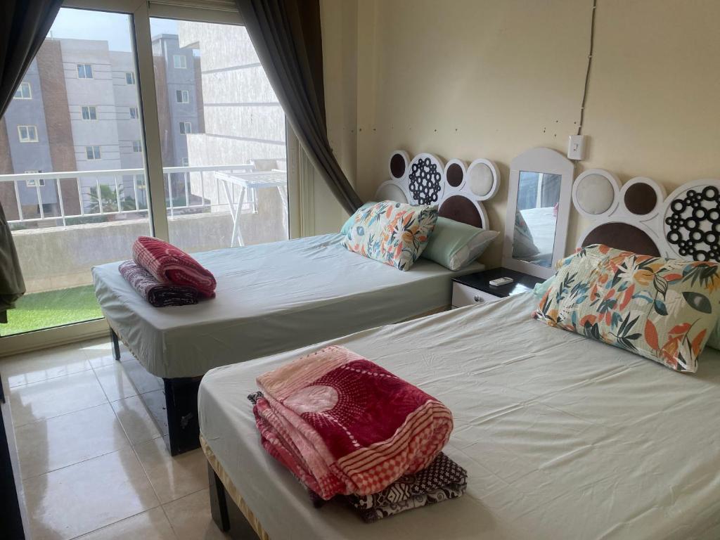 a bedroom with two beds and a large window at شقه فندقيه فاخرة بقرية سياحية متكاملة الخدمات شاطيء رملي وحمامات سباحة واكوابارك على بعد دقائق من مطروح in Marsa Matruh