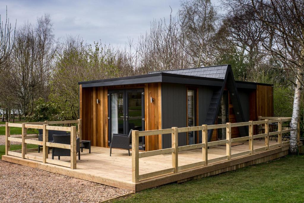 a cabin with a black roof and a wooden deck at Sutton Cabins in Stowey