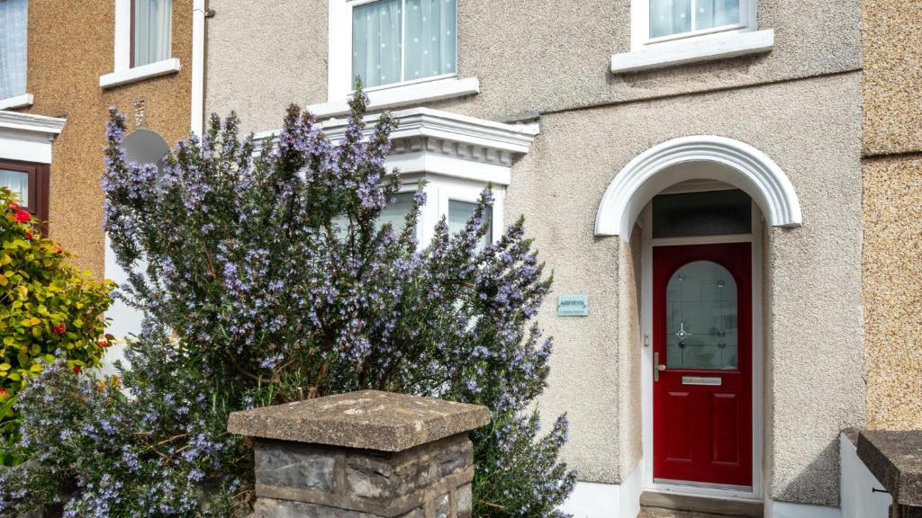 a house with a red door and a bush with purple flowers at Arfryn in The Mumbles