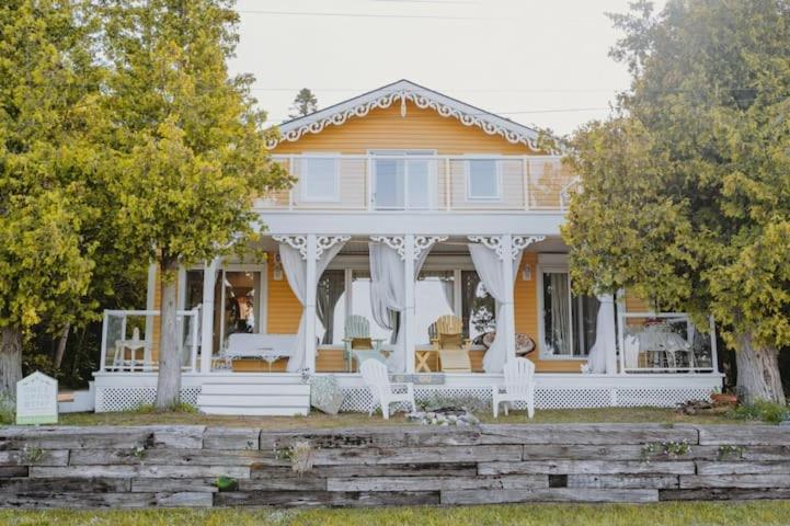 Casa amarilla con porche blanco y sillas blancas en Hot Tub Waterfront Cottage - Near Sauble beach, en Wiarton